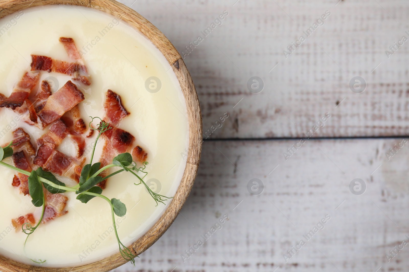 Photo of Delicious potato soup with bacon and microgreens in bowl on wooden table, top view. Space for text