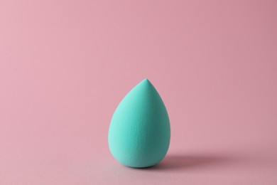 Photo of One turquoise makeup sponge on pink background