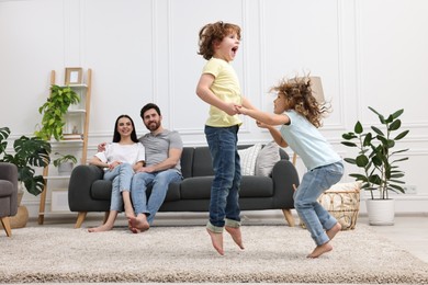 Photo of Happy children dancing while their parents looking at them in room