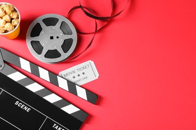 Photo of Clapperboard, popcorn, movie ticket and film reel on red background, top view. Space for text