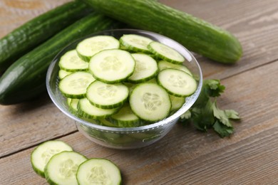 Cut cucumber in glass bowl, fresh vegetables and parsley on wooden table, closeup