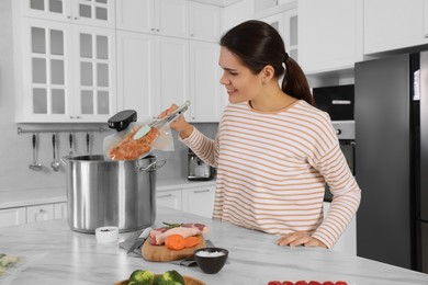 Woman putting vacuum packed meat into pot with sous vide cooker in kitchen. Thermal immersion circulator