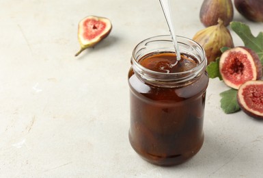 Jar of tasty sweet jam and fresh figs on light table, space for text