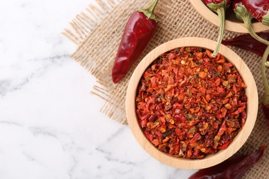 Photo of Chili pepper flakes and pods on white marble table, top view. Space for text