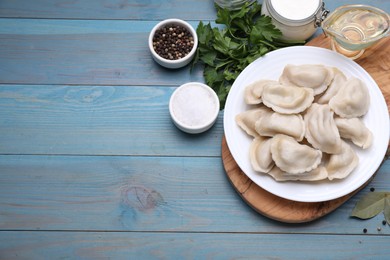 Delicious dumplings (varenyky) with potatoes served on light blue wooden table, flat lay. Space for text