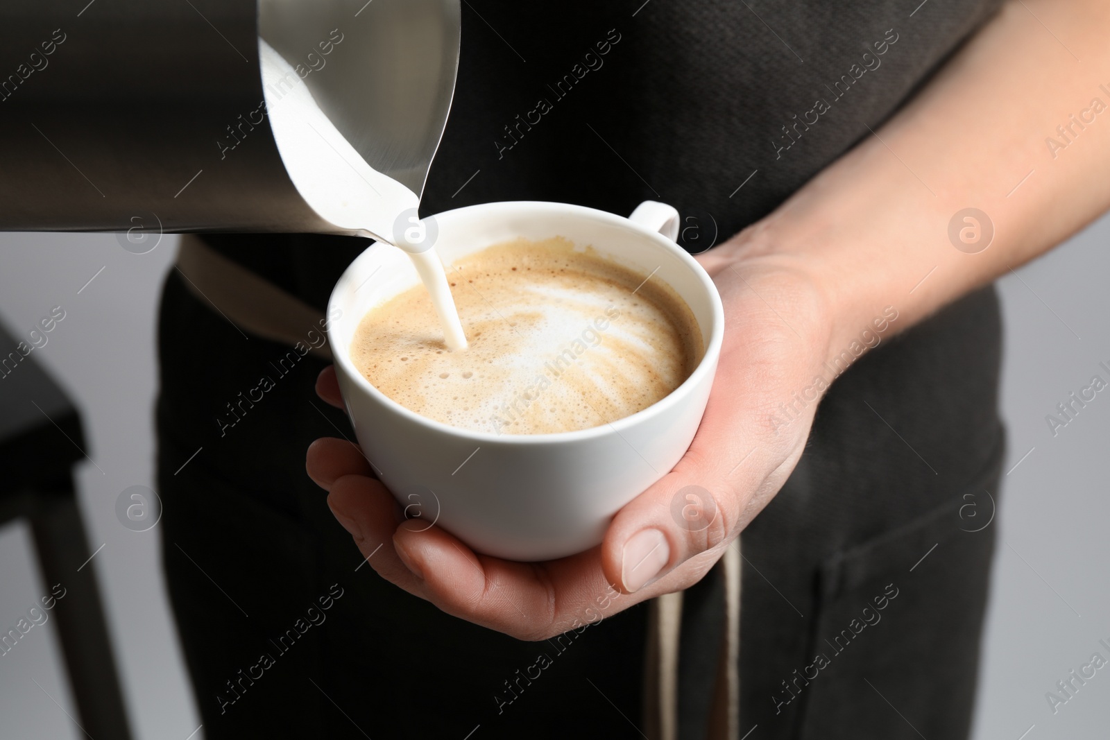 Photo of Woman pouring milk into cup of coffee on grey background, closeup