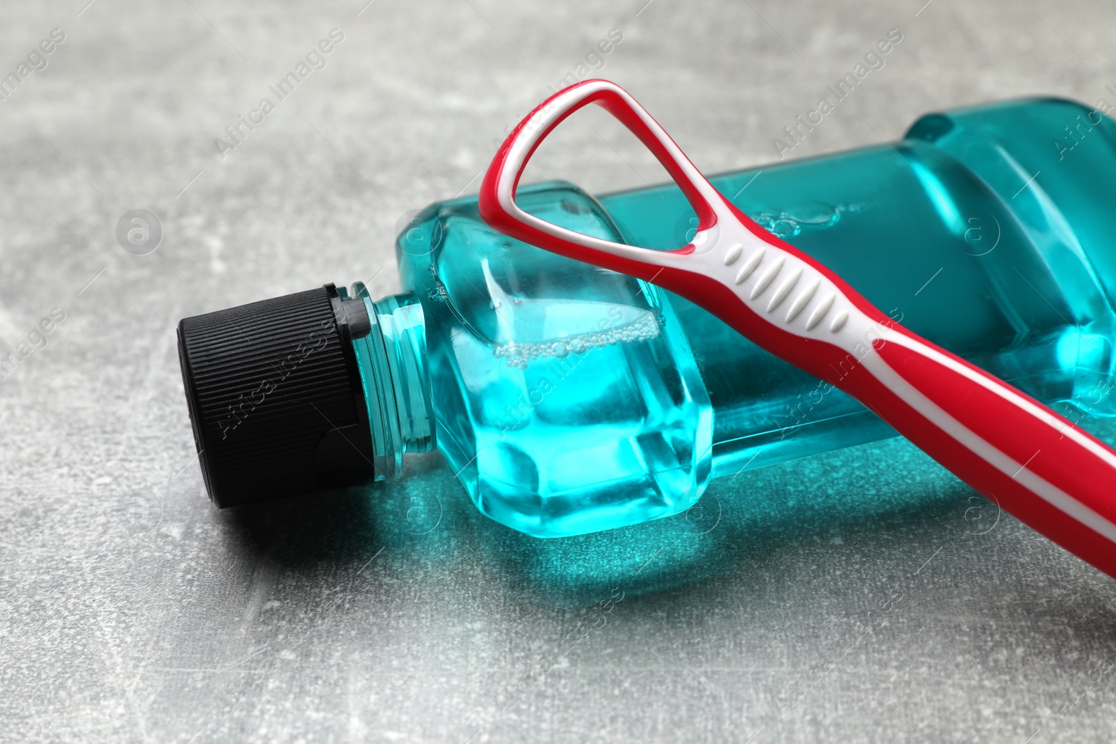 Photo of Red tongue cleaner and mouthwash on grey table, closeup