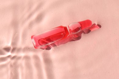 Skincare ampoule in water on pink background, top view