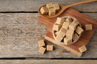 Photo of Bowl and spoon with brown sugar cubes on wooden table, above view. Space for text