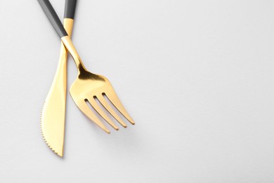 Stylish cutlery. Golden knife and fork on gray background, closeup. Space for text