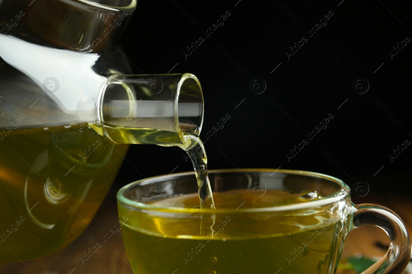 Photo of Pouring green tea into cup on dark background, closeup