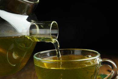 Pouring green tea into cup on dark background, closeup