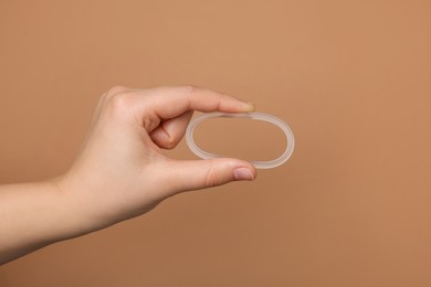 Woman holding diaphragm vaginal contraceptive ring on light brown background, closeup