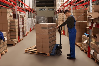 Photo of Worker pulling manual pallet truck with boxes wrapped in stretch film at warehouse