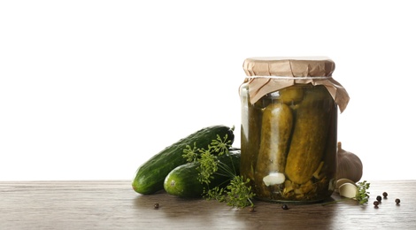 Photo of Glass jar of pickled cucumbers on wooden table against white background. Space for text