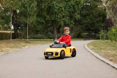 Cute little boy driving children's car outdoors. Space for text