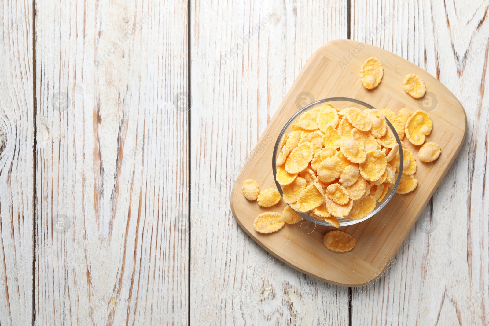 Photo of Glass bowl of tasty crispy corn flakes on white wooden table, top view. Space for text