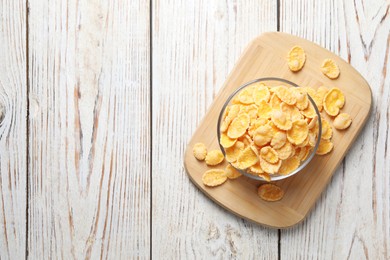 Photo of Glass bowl of tasty crispy corn flakes on white wooden table, top view. Space for text