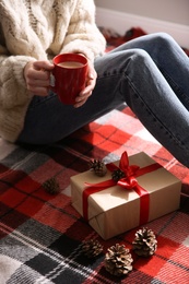 Photo of Woman relaxing with cup of hot winter drink on checkered plaid, closeup. Cozy season