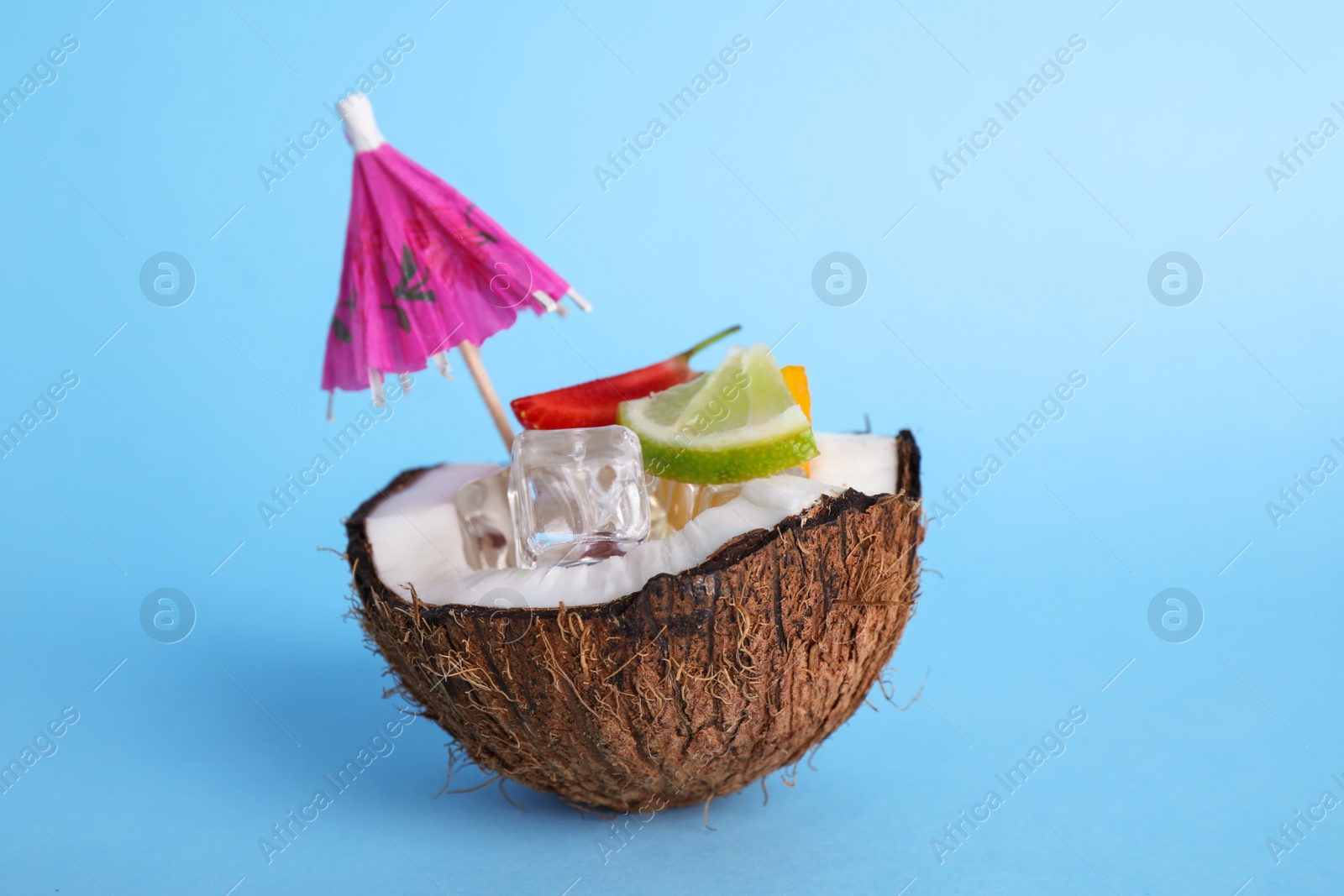 Photo of Summer refreshing cocktail with umbrella in coconut on color background