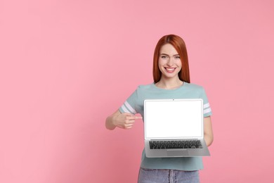 Smiling young woman showing laptop on pink background, space for text