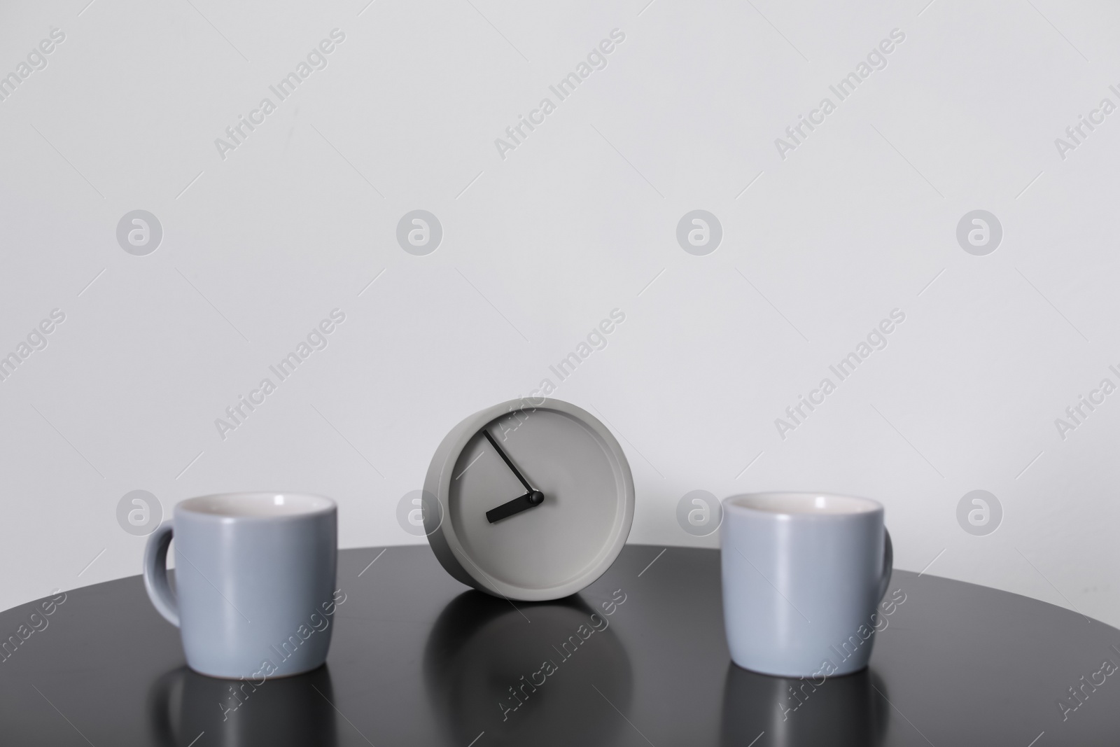 Photo of Analog alarm clock and cups on table. Time of day