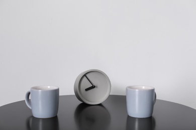 Analog alarm clock and cups on table. Time of day