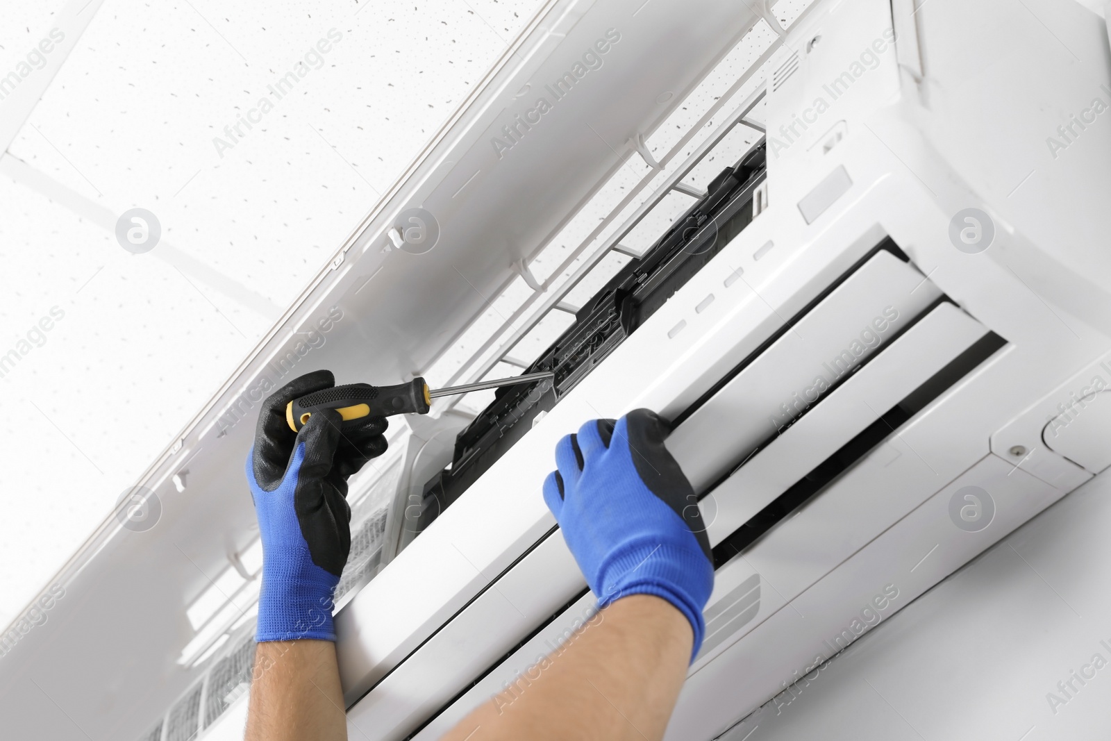 Photo of Male technician fixing modern air conditioner indoors