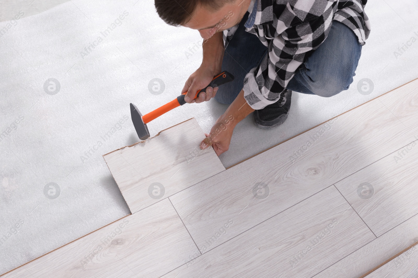 Photo of Professional worker using hammer during installation of new laminate flooring, closeup