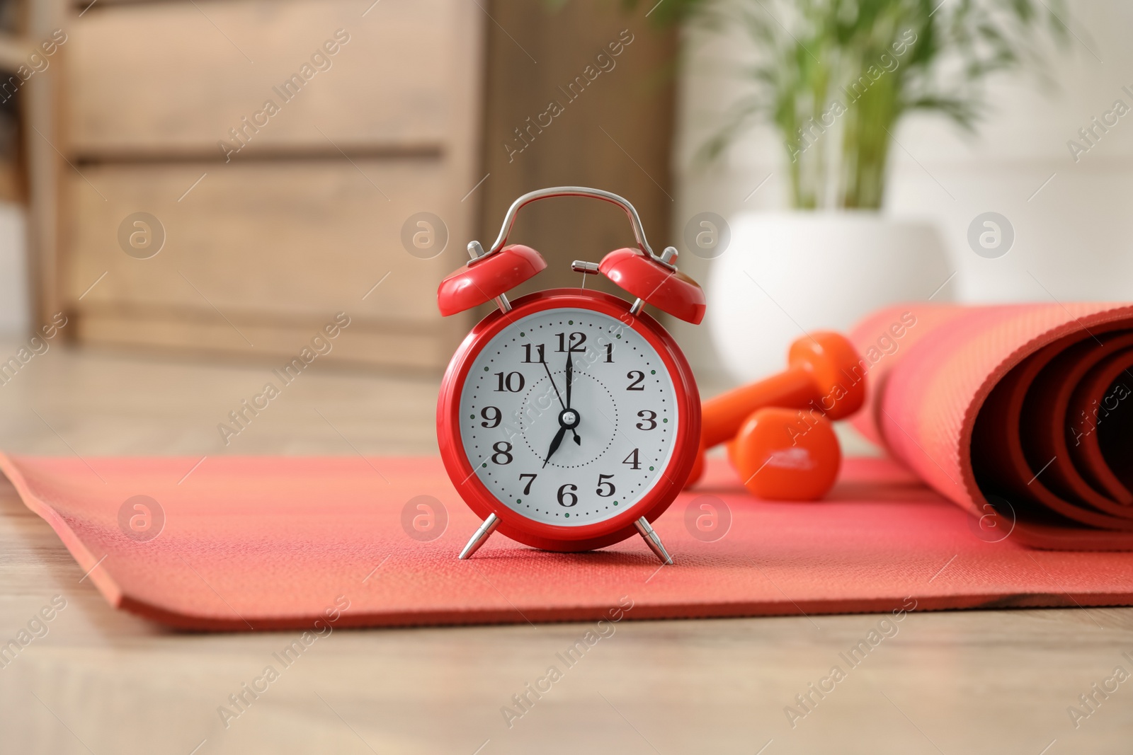 Photo of Alarm clock, yoga mat and dumbbells on wooden floor indoors. Morning exercise