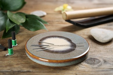 Grey stone coaster with acupuncture needles on wooden table