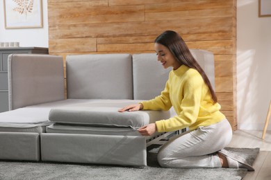 Young woman unfolding sofa into a bed in room. Modern interior