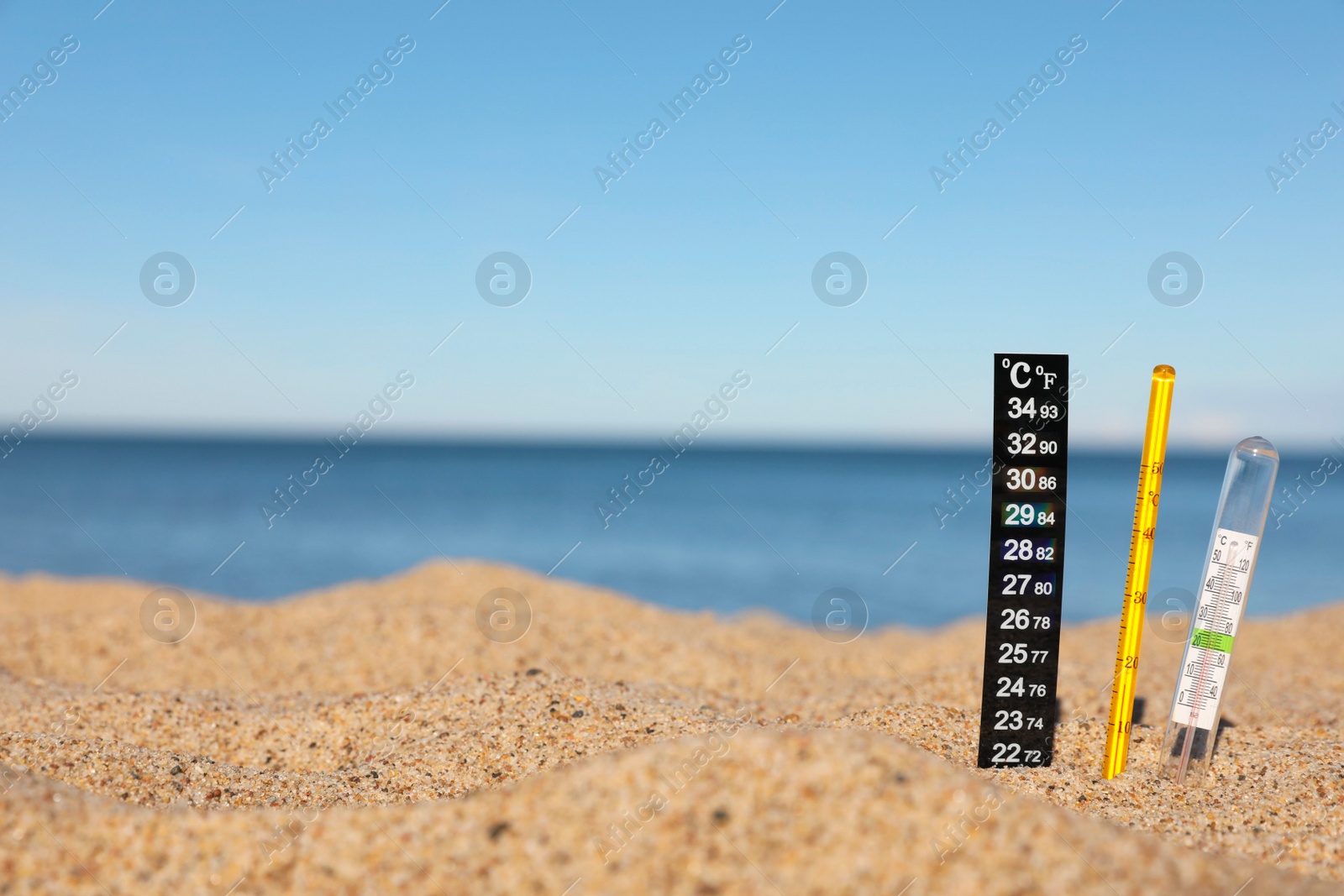 Photo of Weather thermometers in sand near sea, space for text