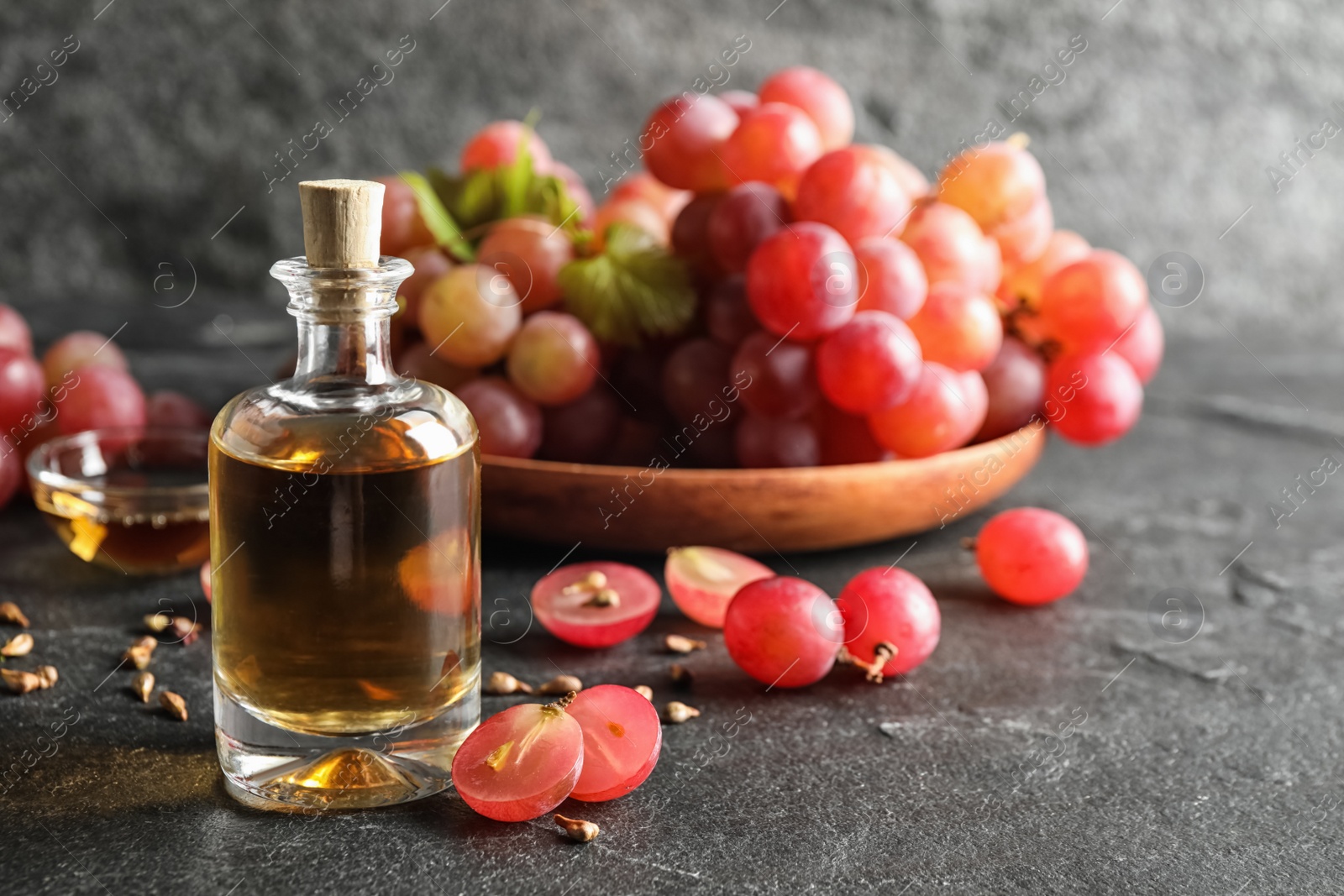 Photo of Organic red grapes, seeds and bottle of natural essential oil on black table. Space for text.