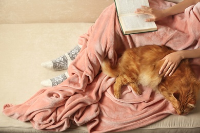 Woman with cute red cat and book on sofa at home, closeup view. Space for text