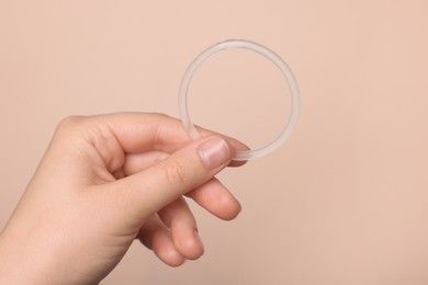 Photo of Woman holding diaphragm vaginal contraceptive ring on beige background, closeup
