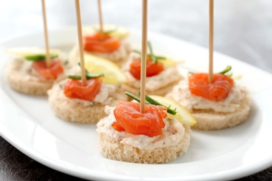 Photo of Canapes with fresh sliced salmon fillet on plate, closeup
