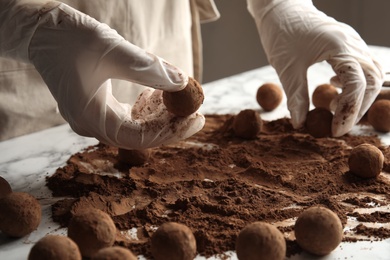 Woman preparing tasty chocolate truffles at table, closeup