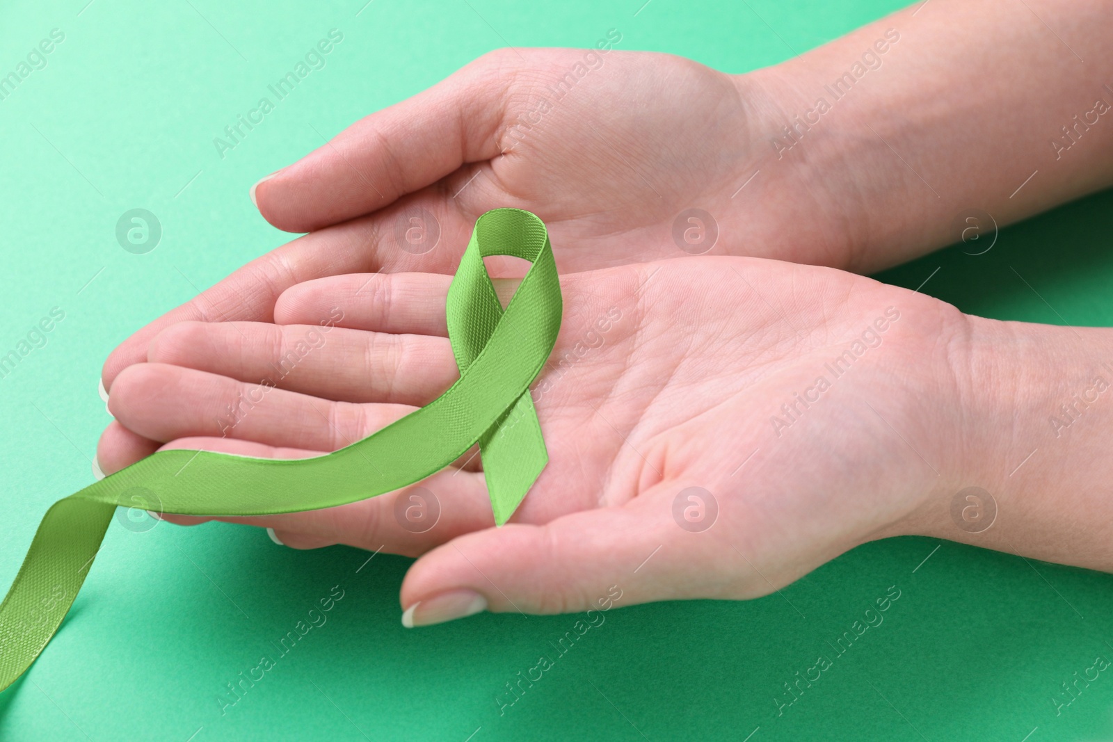 Photo of World Mental Health Day. Woman holding green ribbon on color background, closeup