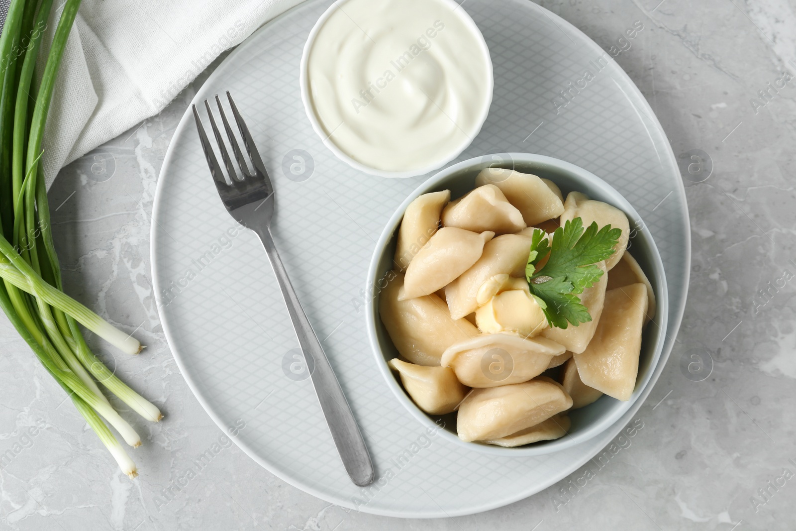 Photo of Delicious cooked dumplings and sour cream on grey marble table, flat lay