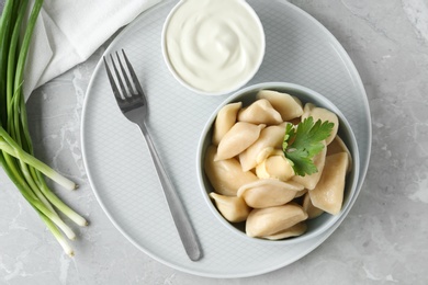 Delicious cooked dumplings and sour cream on grey marble table, flat lay