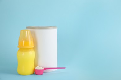 Photo of Blank can of powdered infant formula with feeding bottle and scoop on light blue background, space for text. Baby milk