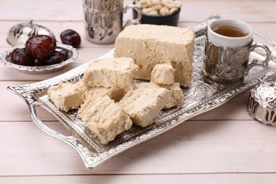 Photo of Pieces of tasty halva, tea and dates on light wooden table, closeup