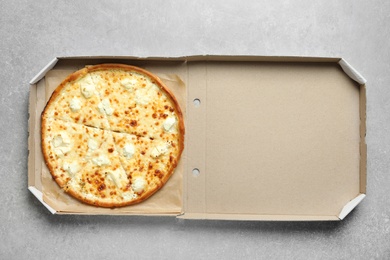Carton box with delicious pizza on grey background, top view