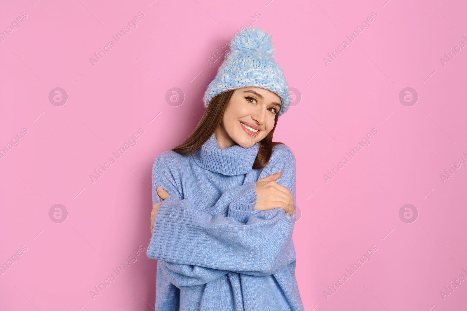 Photo of Young woman wearing warm sweater and hat on pink background. Winter season