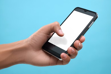 Man using smartphone with blank screen on light blue background, closeup. Mockup for design