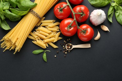 Different types of pasta, spices and products on black background, flat lay. Space for text