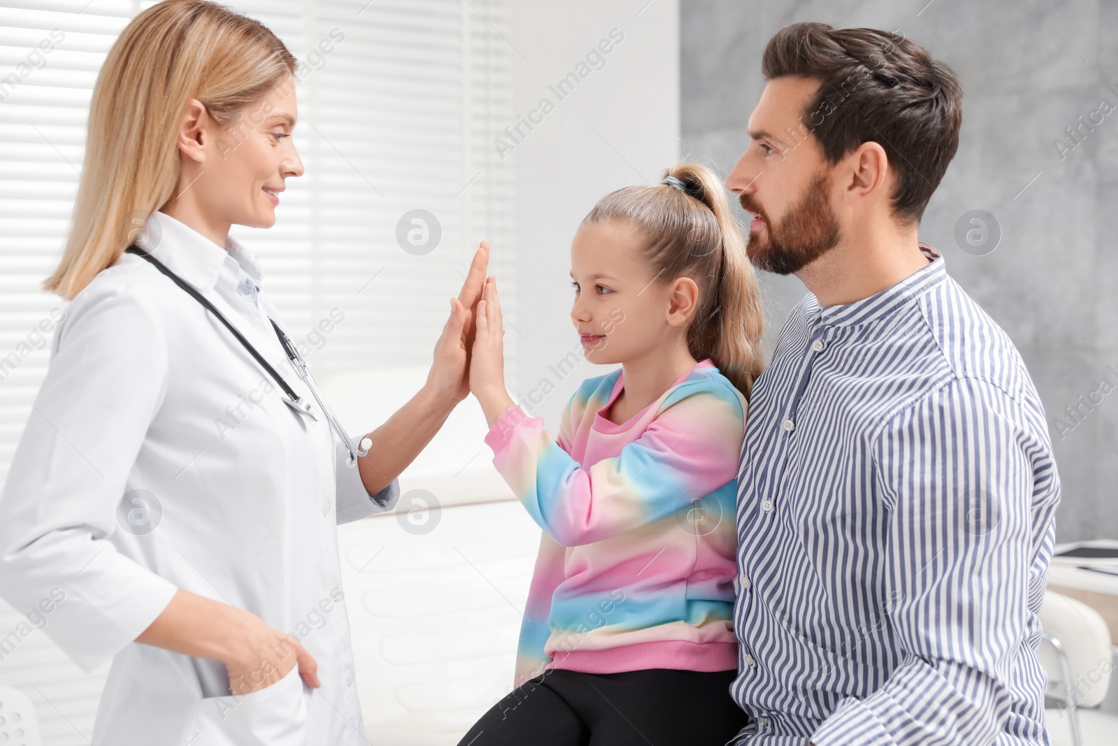 Photo of Happy father and daughter having appointment with doctor. Pediatrician and patient giving high five in clinic