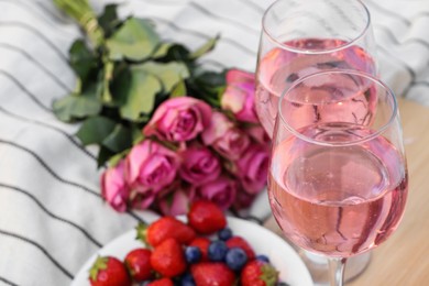 Photo of Glasses of delicious rose wine, flowers and food on white picnic blanket, closeup