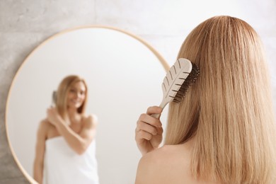 Photo of Woman brushing her hair near mirror in bathroom